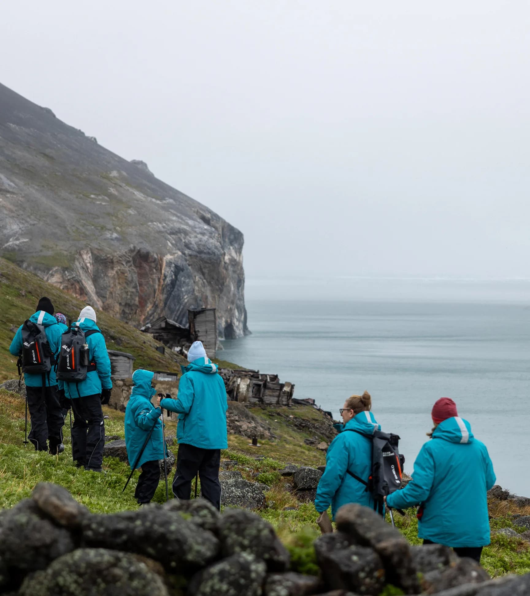 Guests hiking a green coastal slope below sea cliffs