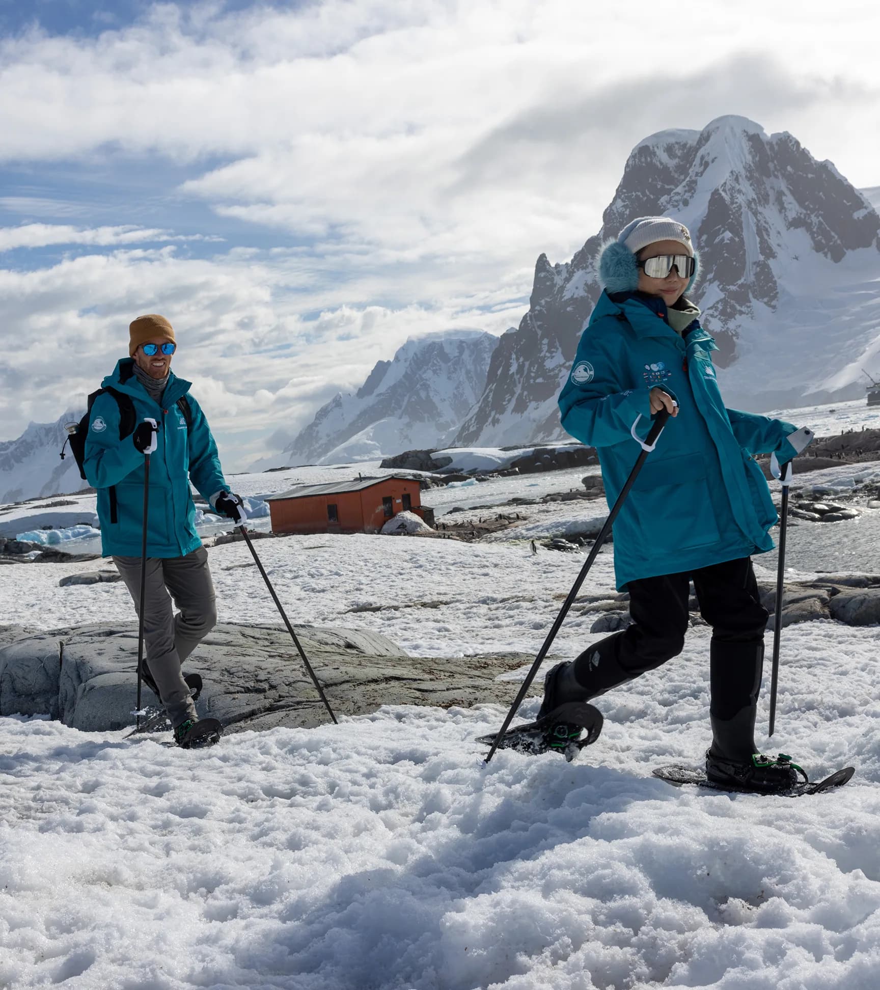 Two guests snowshoeing below jagged snow-covered peaks