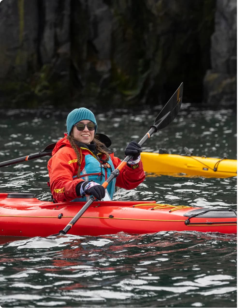 Guest kayaking beside a rock face in expedition gear
